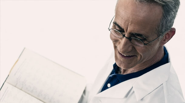 Man with glasses in a lab coat holding an open book
